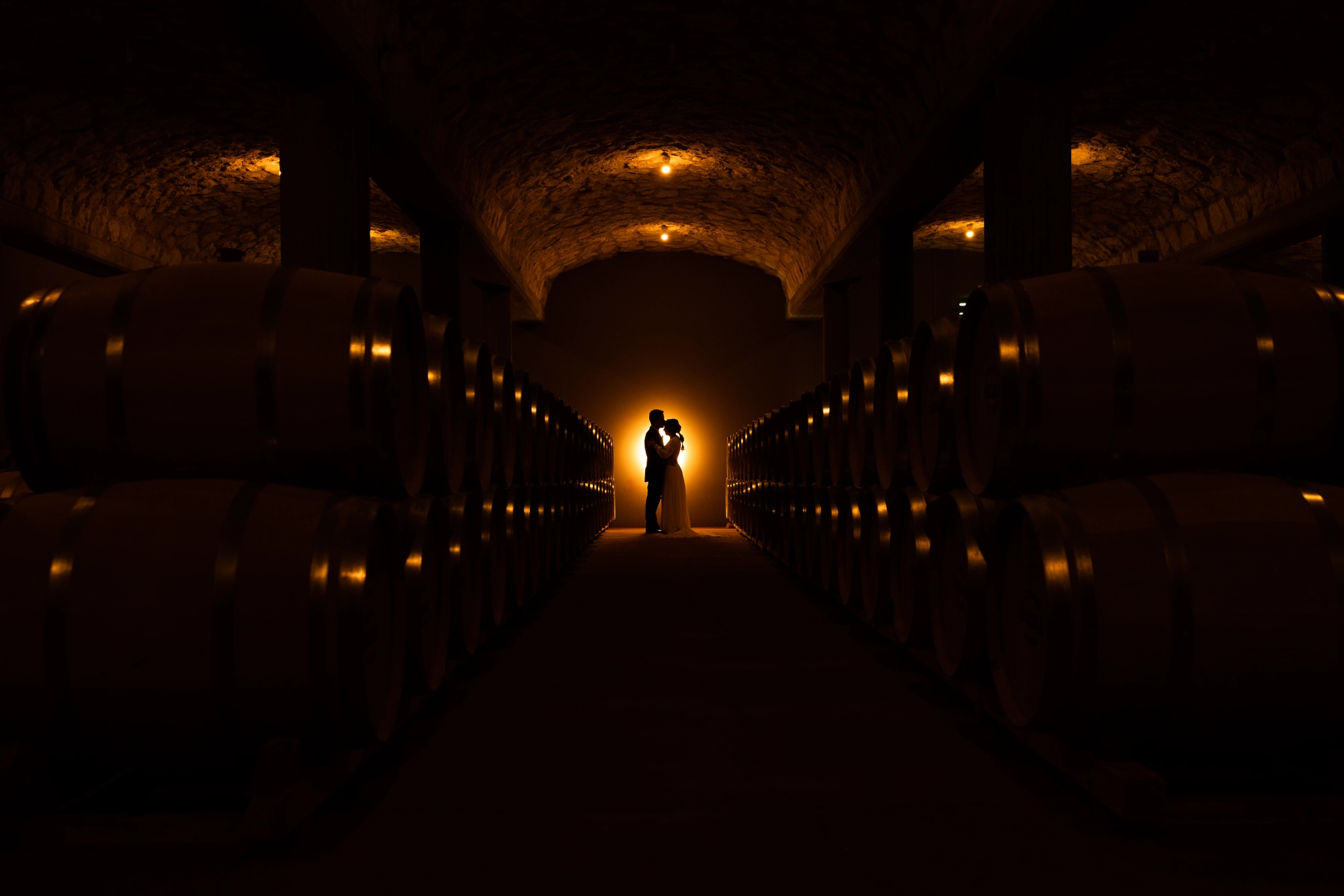 Fotógrafos de boda en Ribera del Duero: pareja a contraluz en la nave de barricas de Bodegas Arzuaga