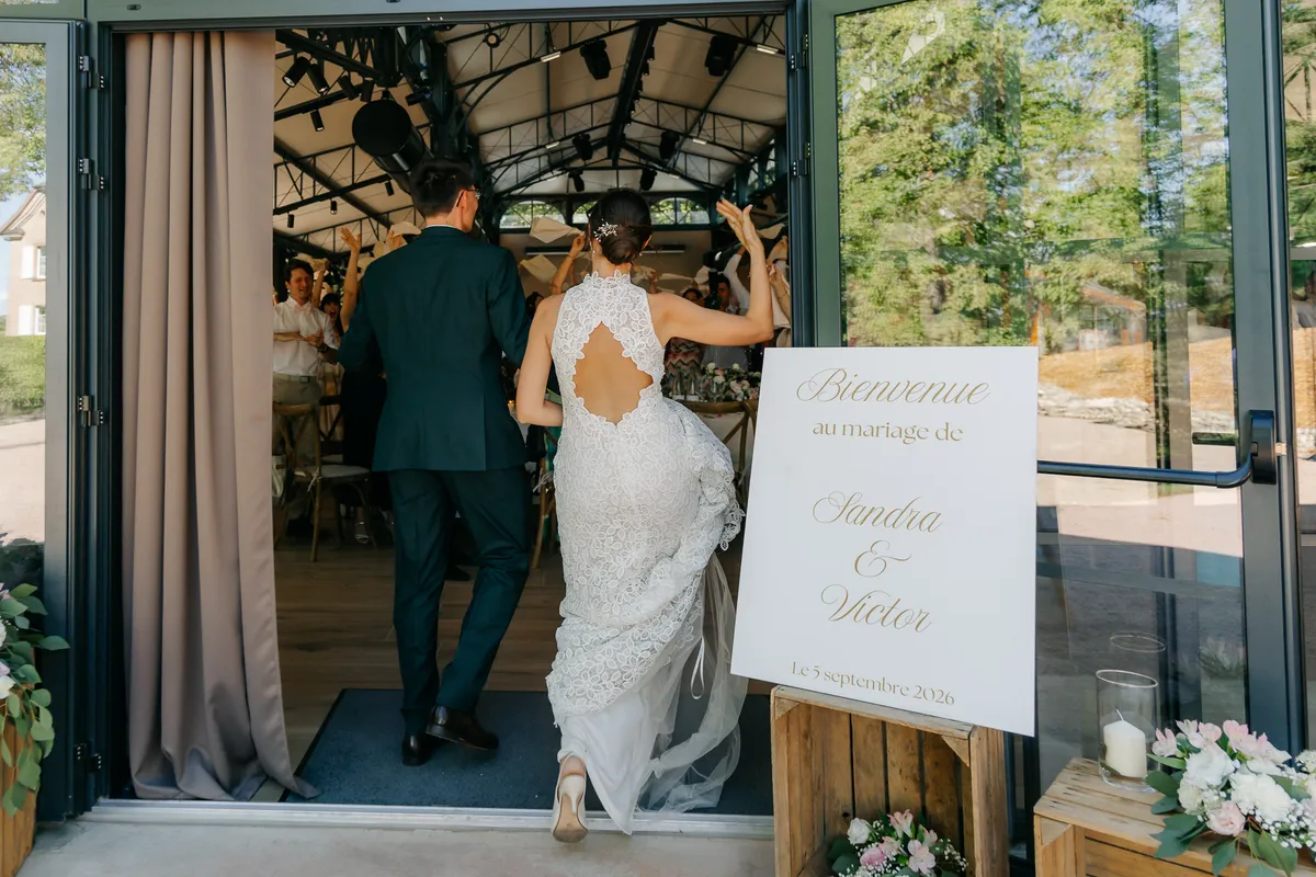 Los novios entrando al invernadero acristalado junto al cartel de bienvenida de la boda de Sandra y Víctor