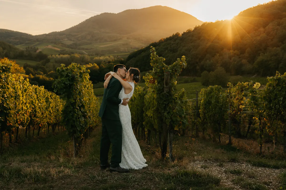 Los novios abrazados entre las viñas de la Alsacia a contraluz, con el sol cayendo tras las montañas