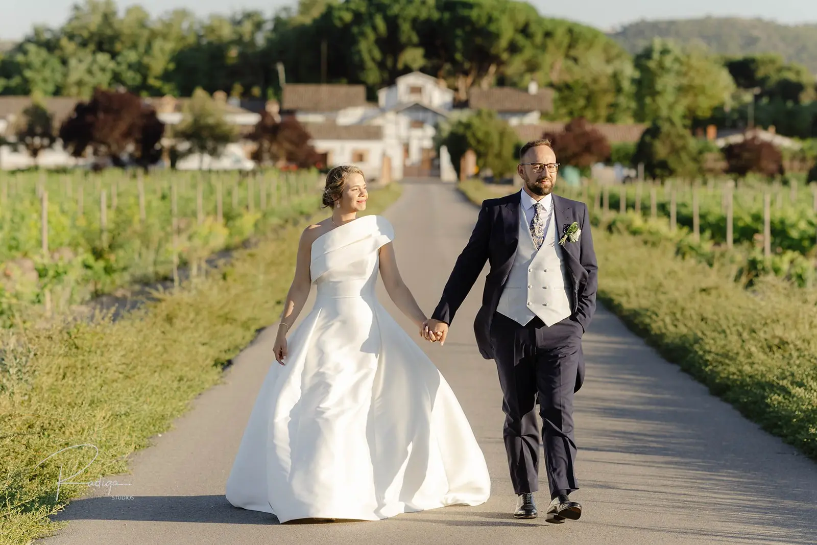 Los novios pasean de la mano por el camino entre viñedos de Dehesa de los Canónigos