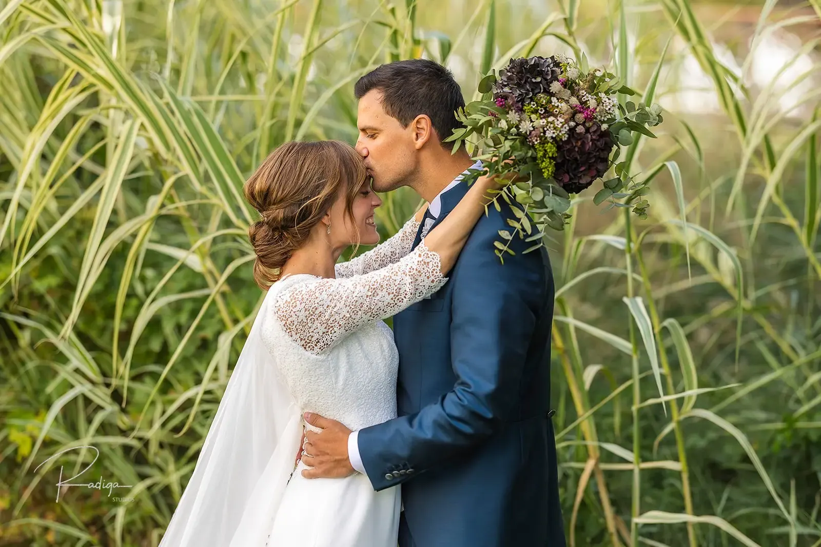 Los novios se besan entre las cañas del jardín del AC Palacio de Santa Ana, con el ramo en alto