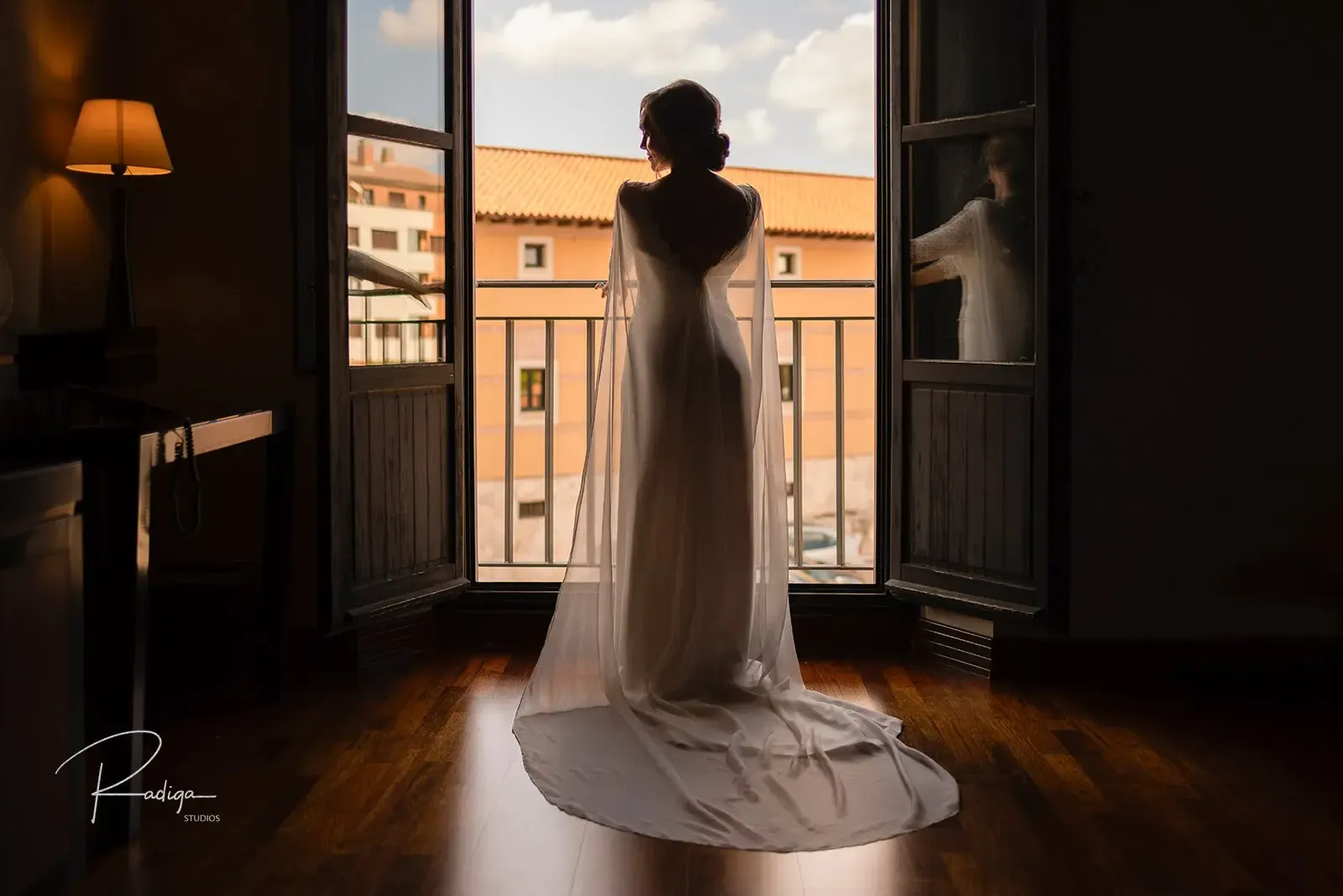 La novia, ya vestida, frente a la ventana abierta de la habitación