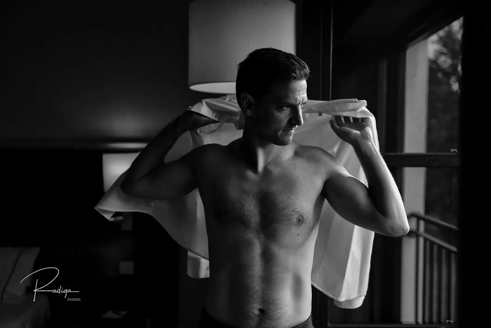 El novio se pone la camisa en la habitación, en blanco y negro