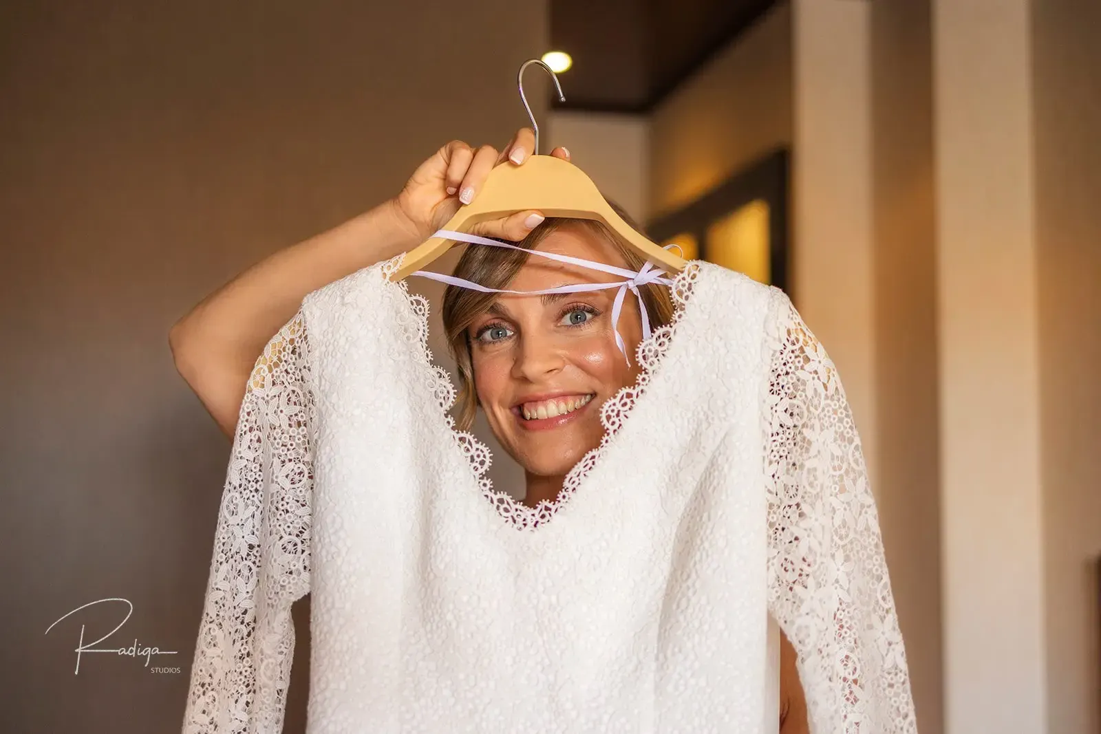 La novia se ríe asomada tras el vestido colgado en la percha