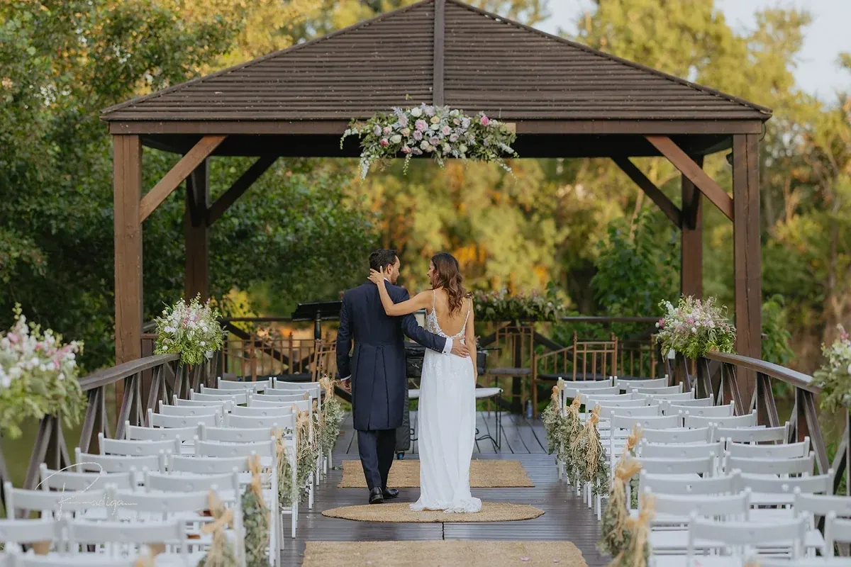 Los novios bajo la pérgola del embarcadero, con las sillas blancas de la ceremonia