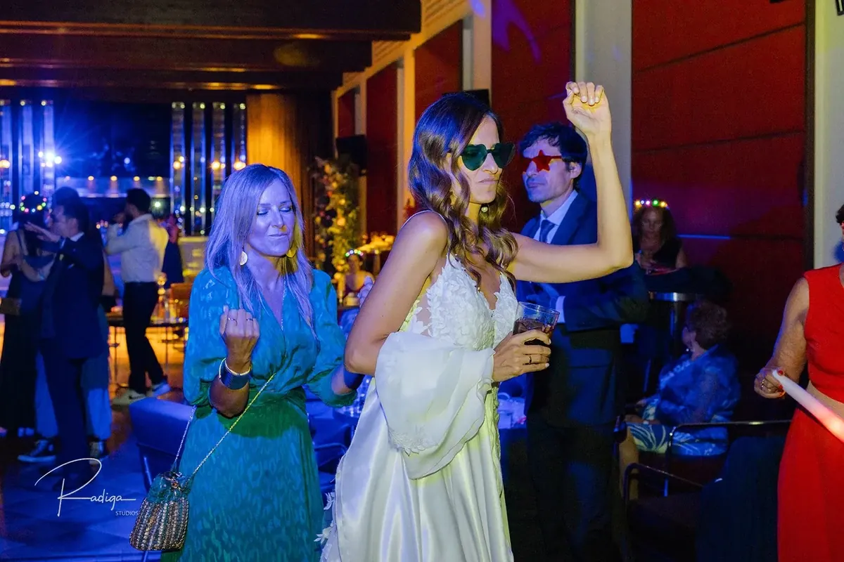 La novia baila con una amiga con gafas de fiesta
