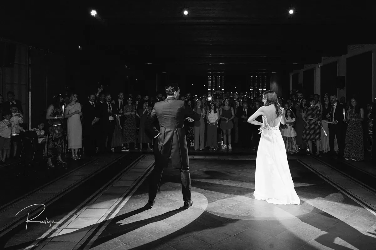 Los novios bailan en la pista rodeados de invitados, en blanco y negro