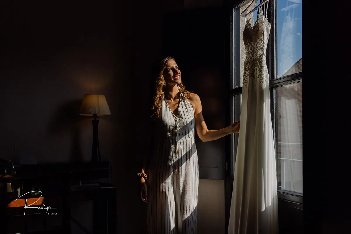 La novia junto al vestido colgado en la ventana de la habitación