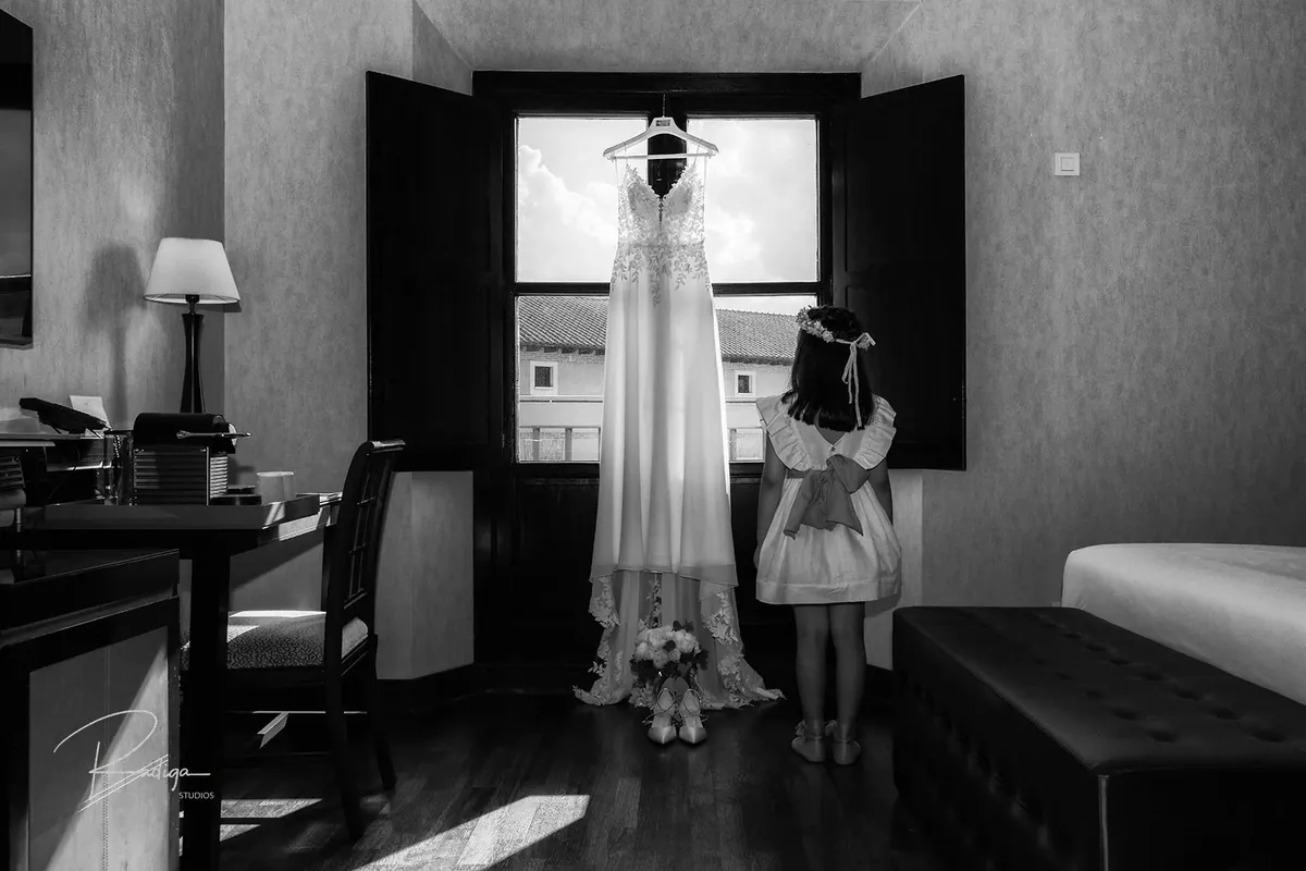 El vestido de novia junto a la ventana de la habitación y una niña que lo mira