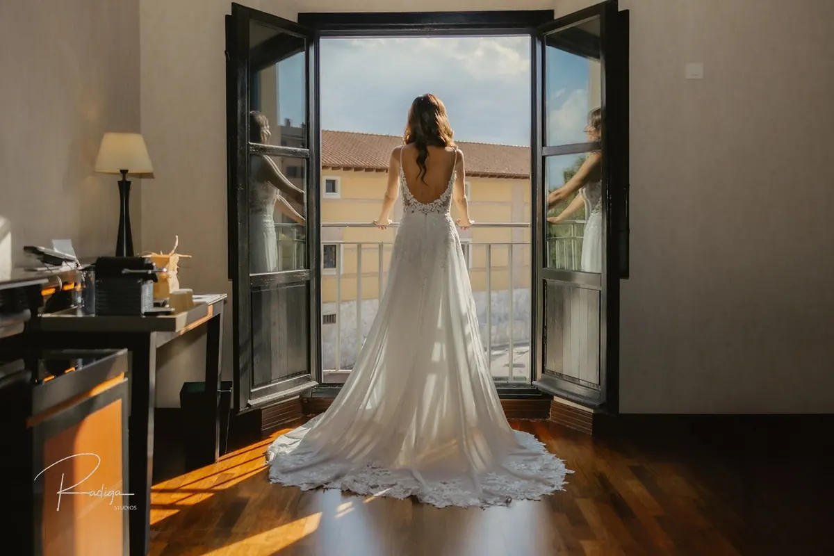 La novia de espaldas frente al balcón abierto de la habitación