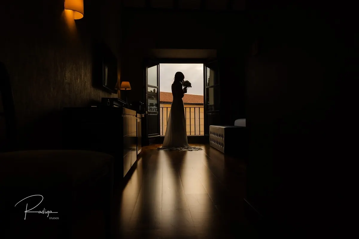 La novia en el pasillo en penumbra, recortada contra la luz del balcón