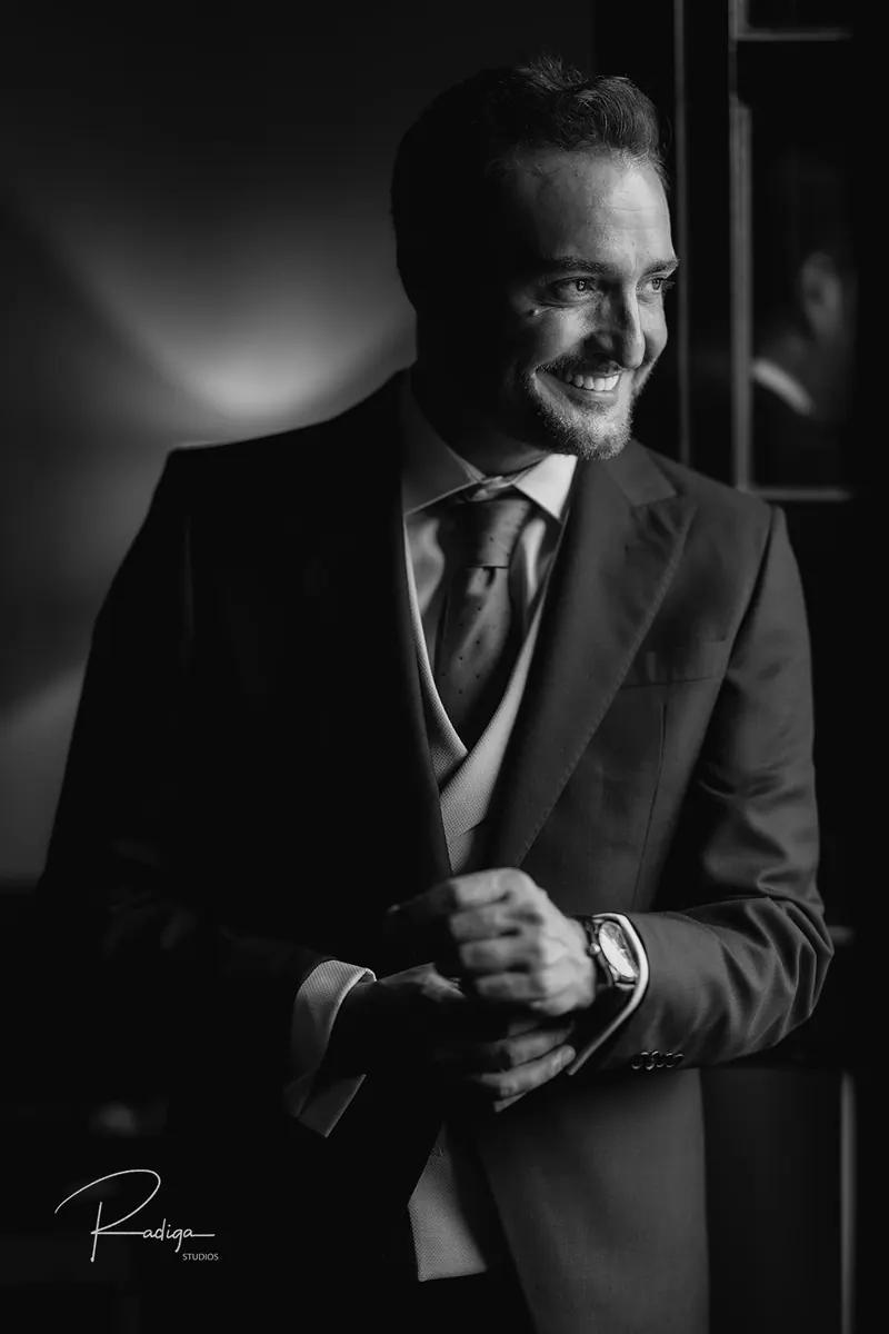 Retrato del novio con chaleco y corbata junto a la ventana, en blanco y negro