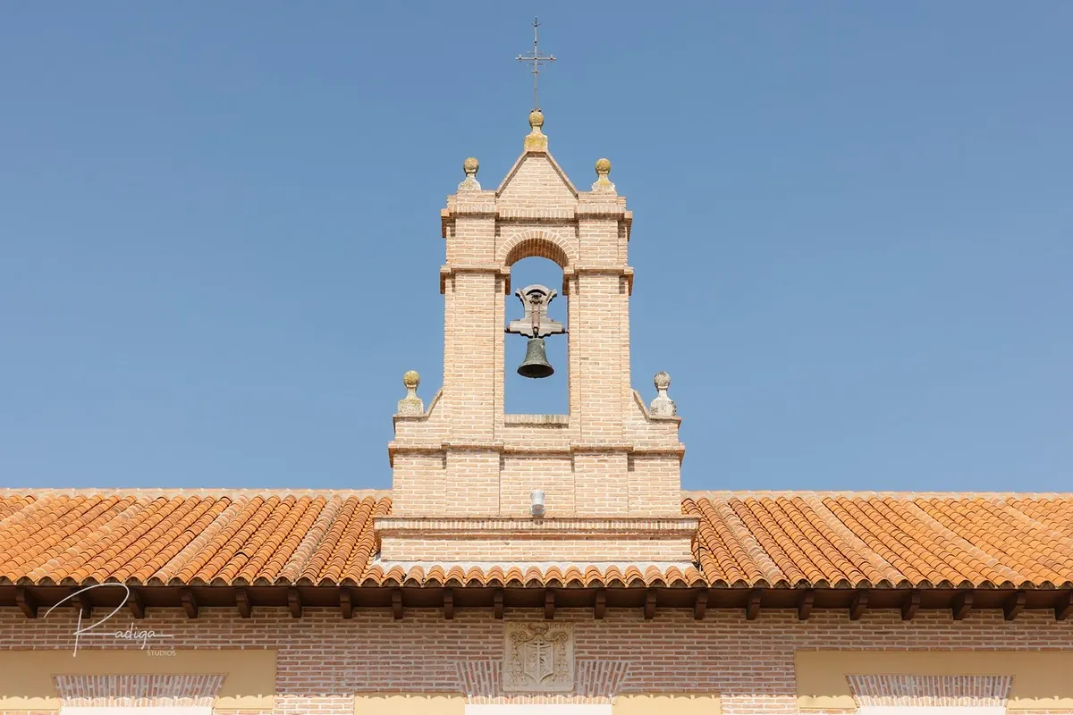 La espadaña con campana del AC Palacio de Santa Ana recortada contra el cielo azul