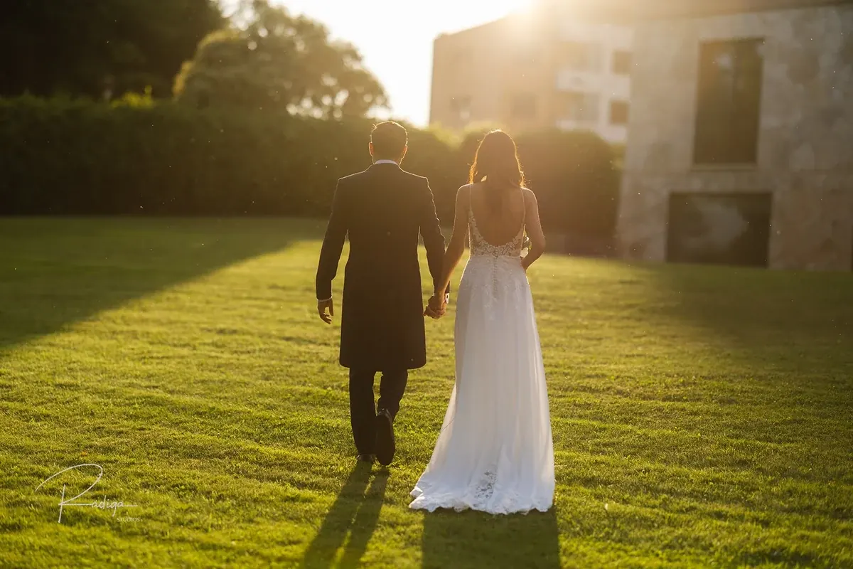 Los novios caminan de la mano por el jardín al atardecer