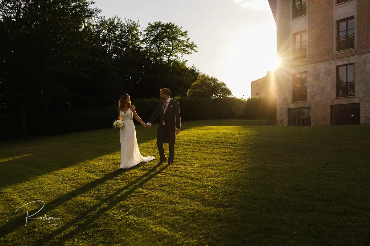 Los novios en el césped con el sol del atardecer detrás del palacio