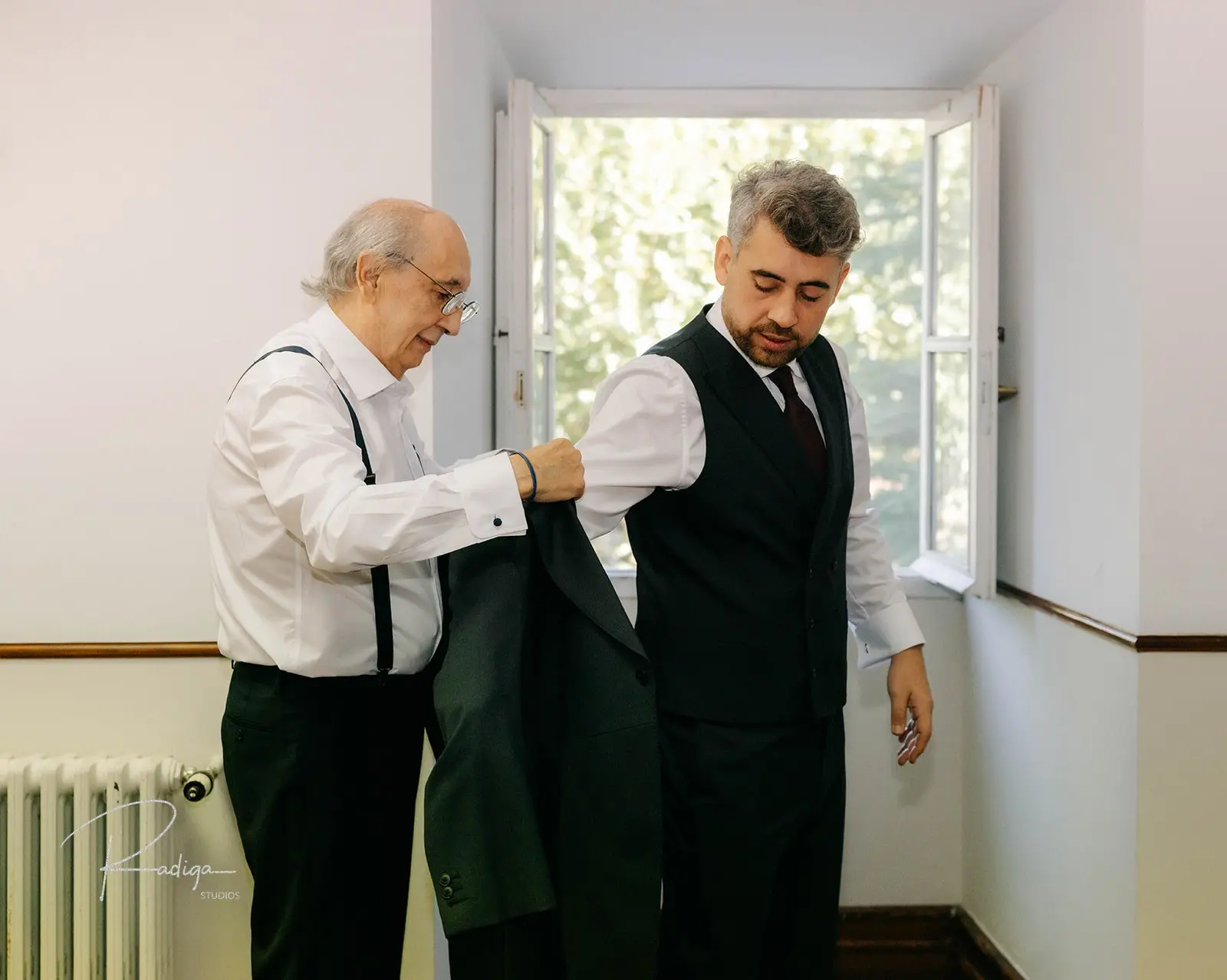 El novio termina de vestirse junto a la ventana ayudado por su familia