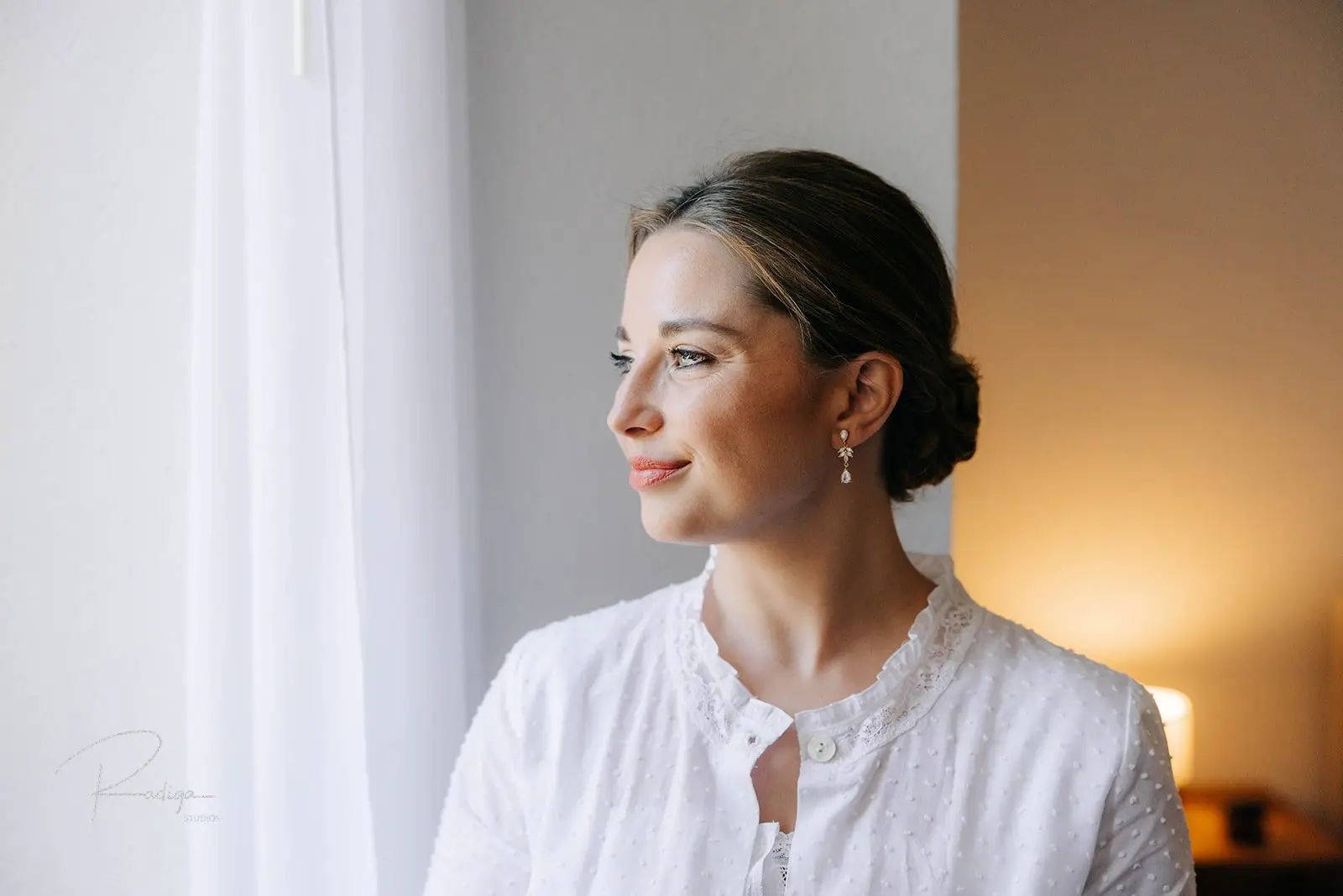 Retrato de la novia junto a la ventana durante los preparativos