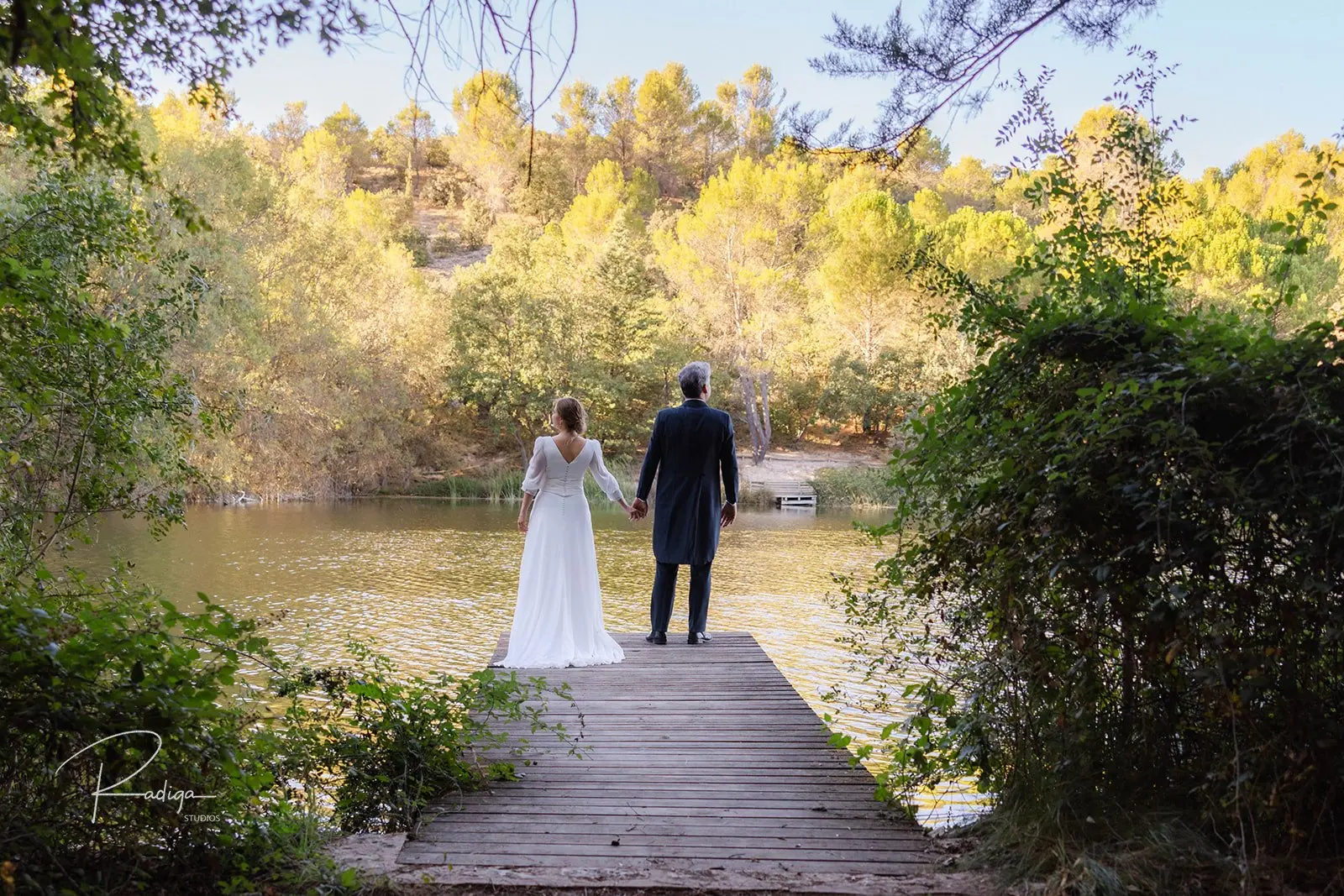 Los novios de espaldas en un embarcadero de madera junto al agua