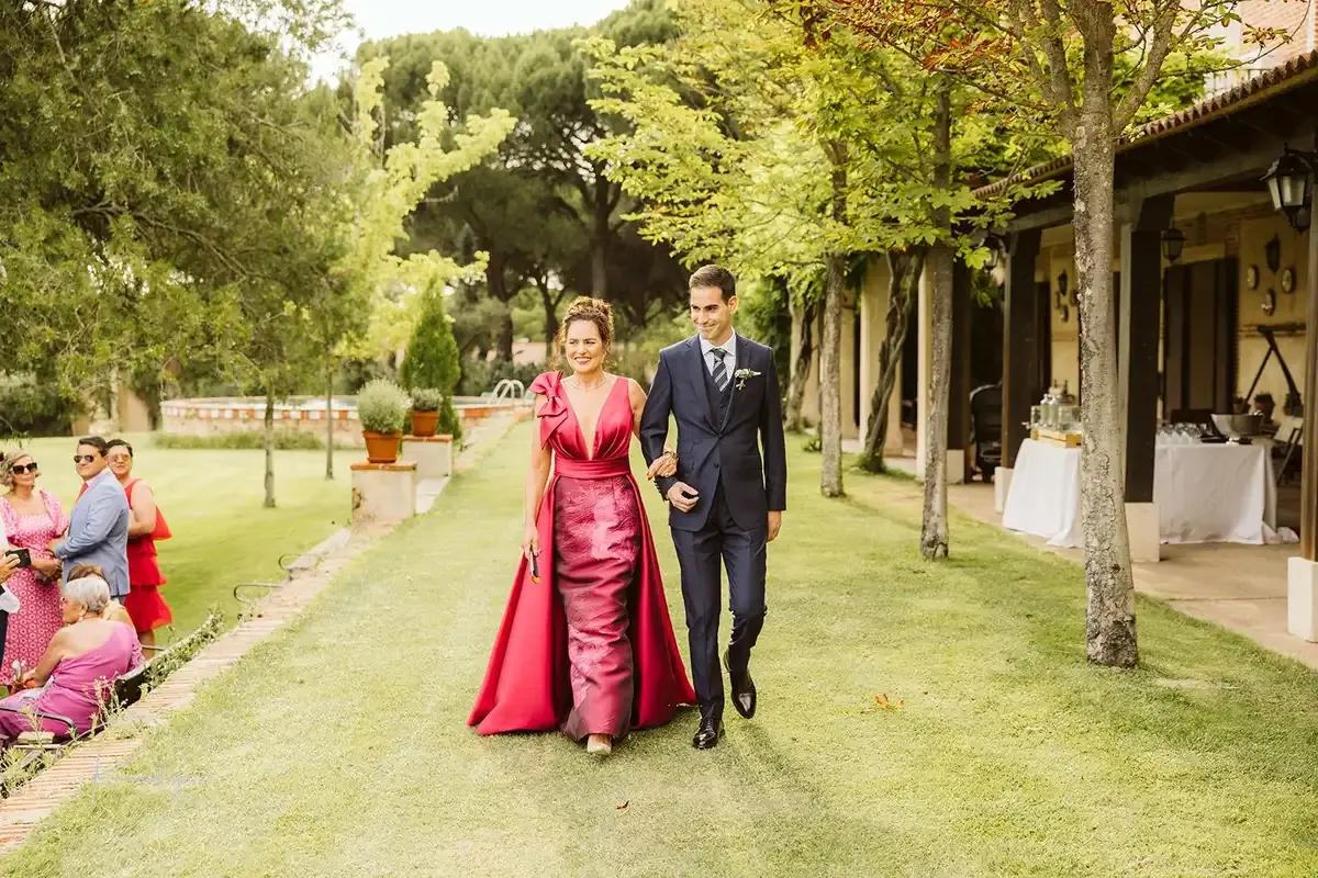 El novio camina hacia la ceremonia del brazo de la madrina, vestida de rojo