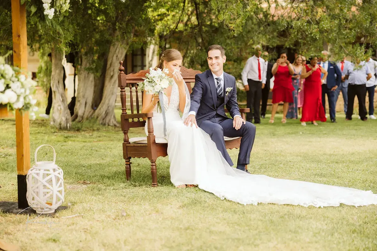 Los novios sentados en un banco de madera durante la ceremonia al aire libre