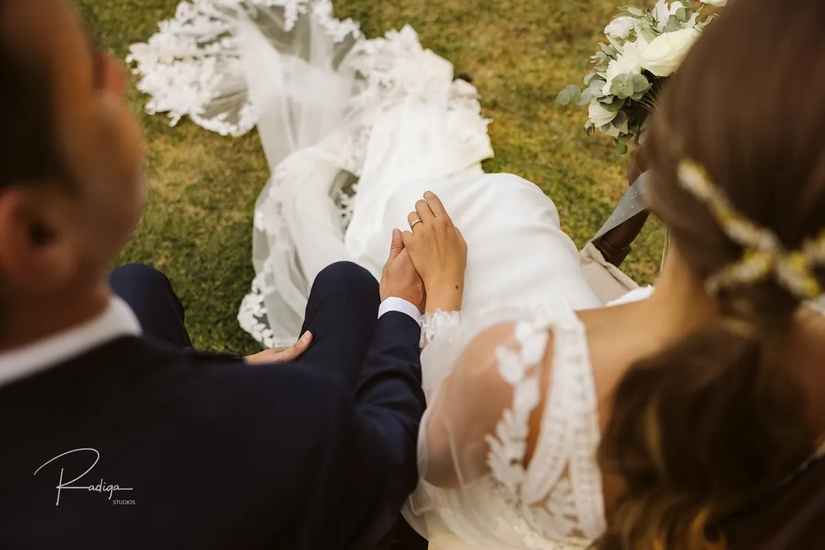 Los novios de la mano, vistos desde detrás, con el velo sobre la hierba