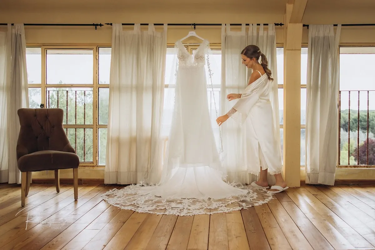 La novia junto a su vestido colgado frente a la ventana