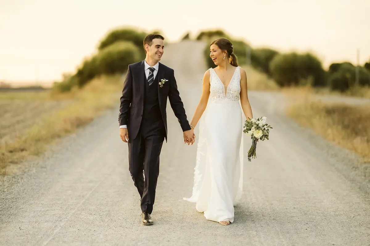 Los novios caminan de la mano por un camino de tierra