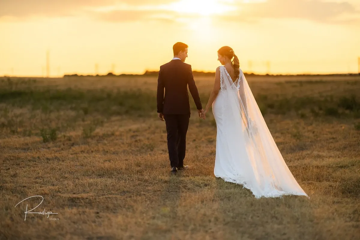 Los novios pasean por el campo al atardecer con el velo al viento