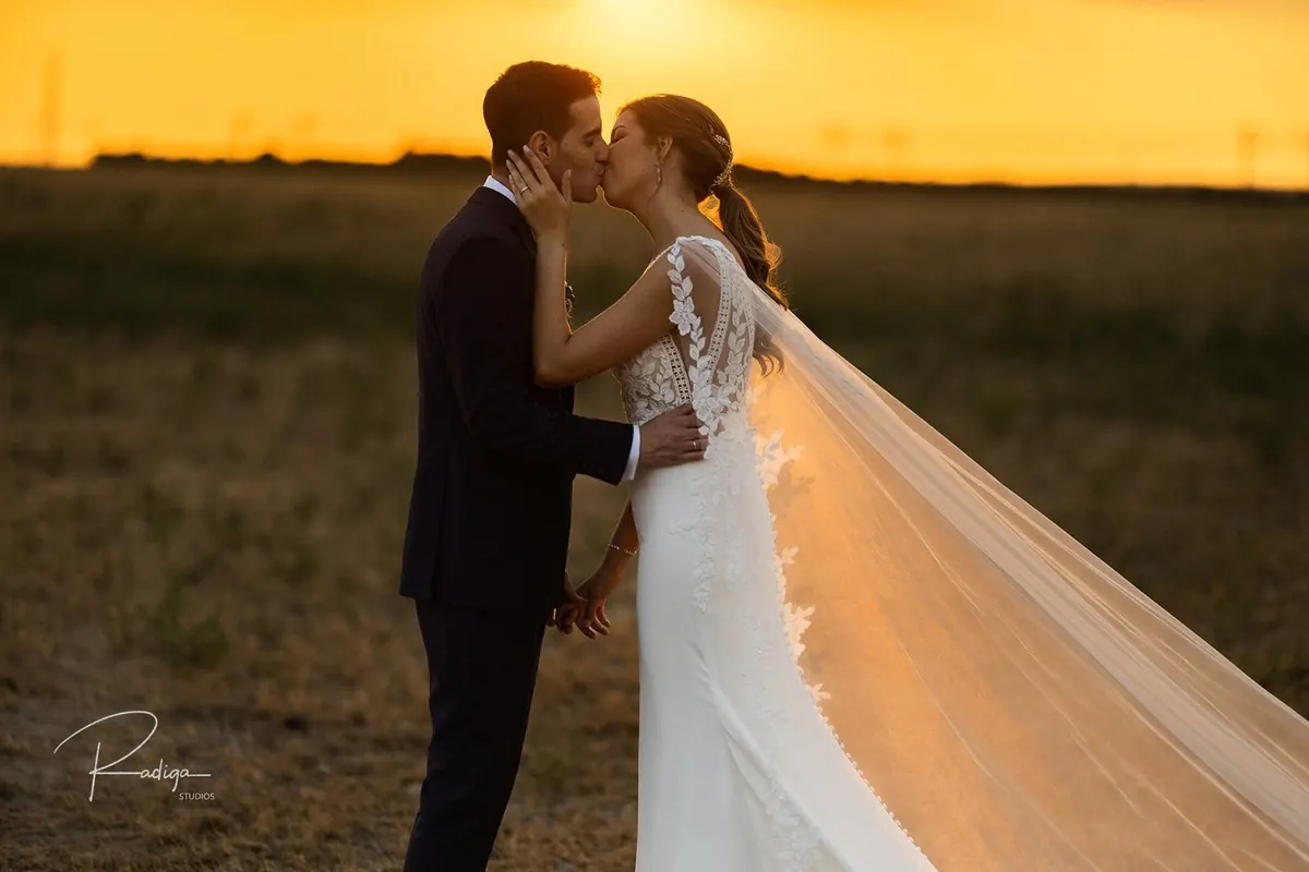 Los novios se besan al atardecer con el velo al viento en un campo junto a la Posada Real del Pinar