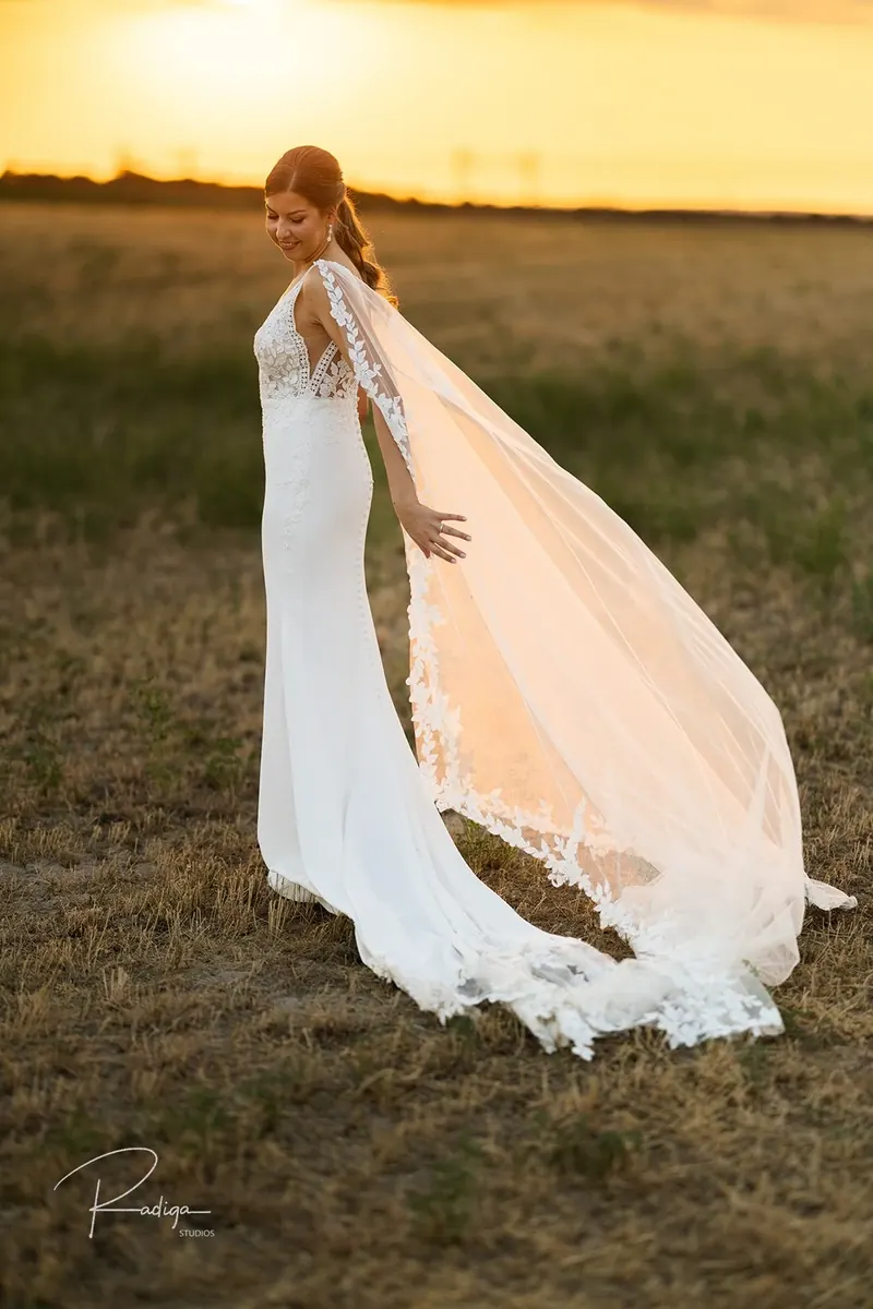 La novia de espaldas con el velo al viento y el sol poniéndose