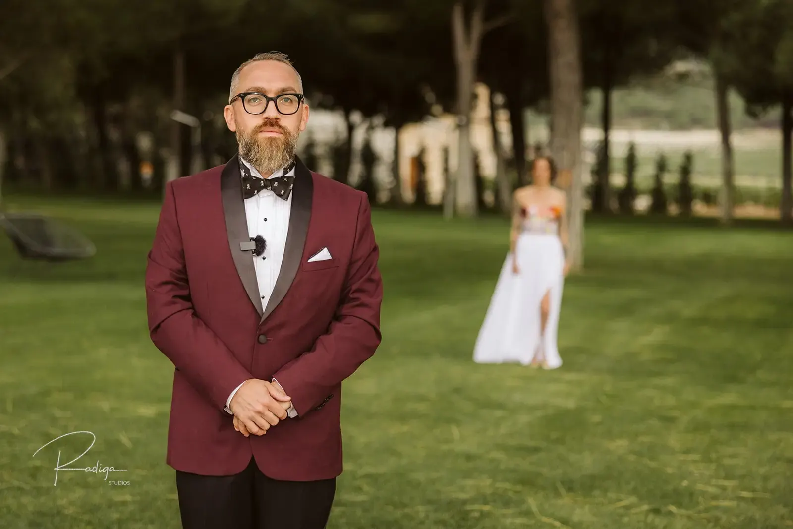 The groom waits in the garden as the bride walks up behind him for the first look