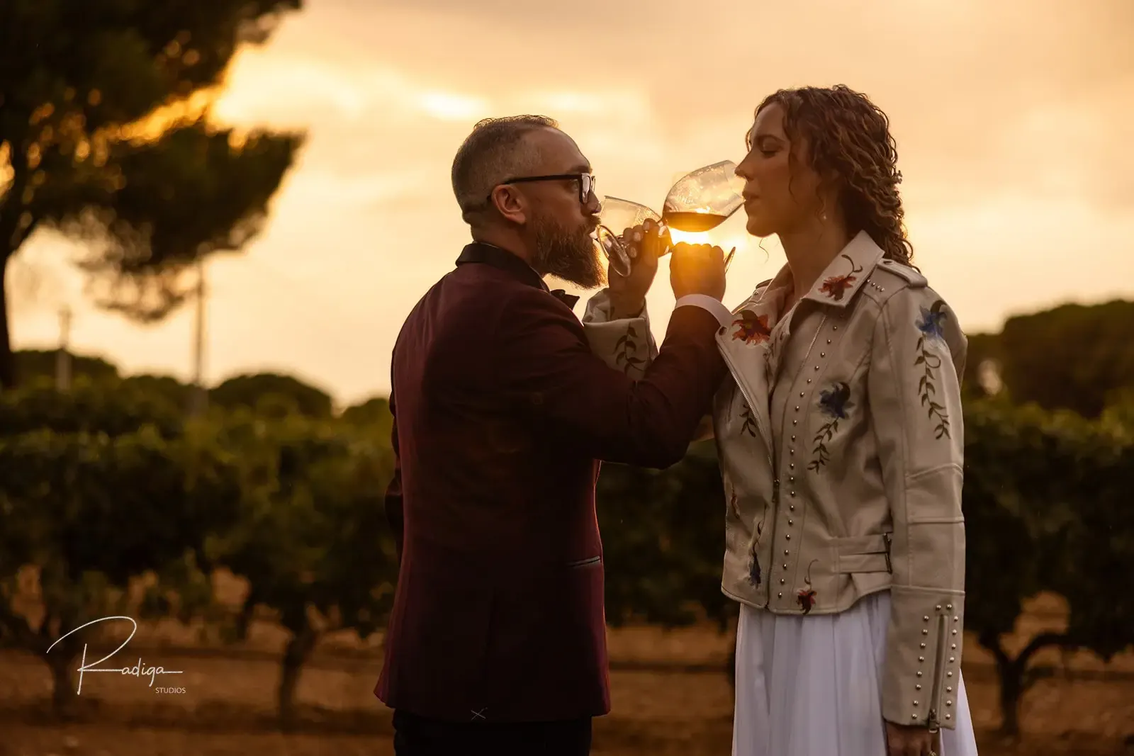 The couple drinking red wine among the vines in the golden light