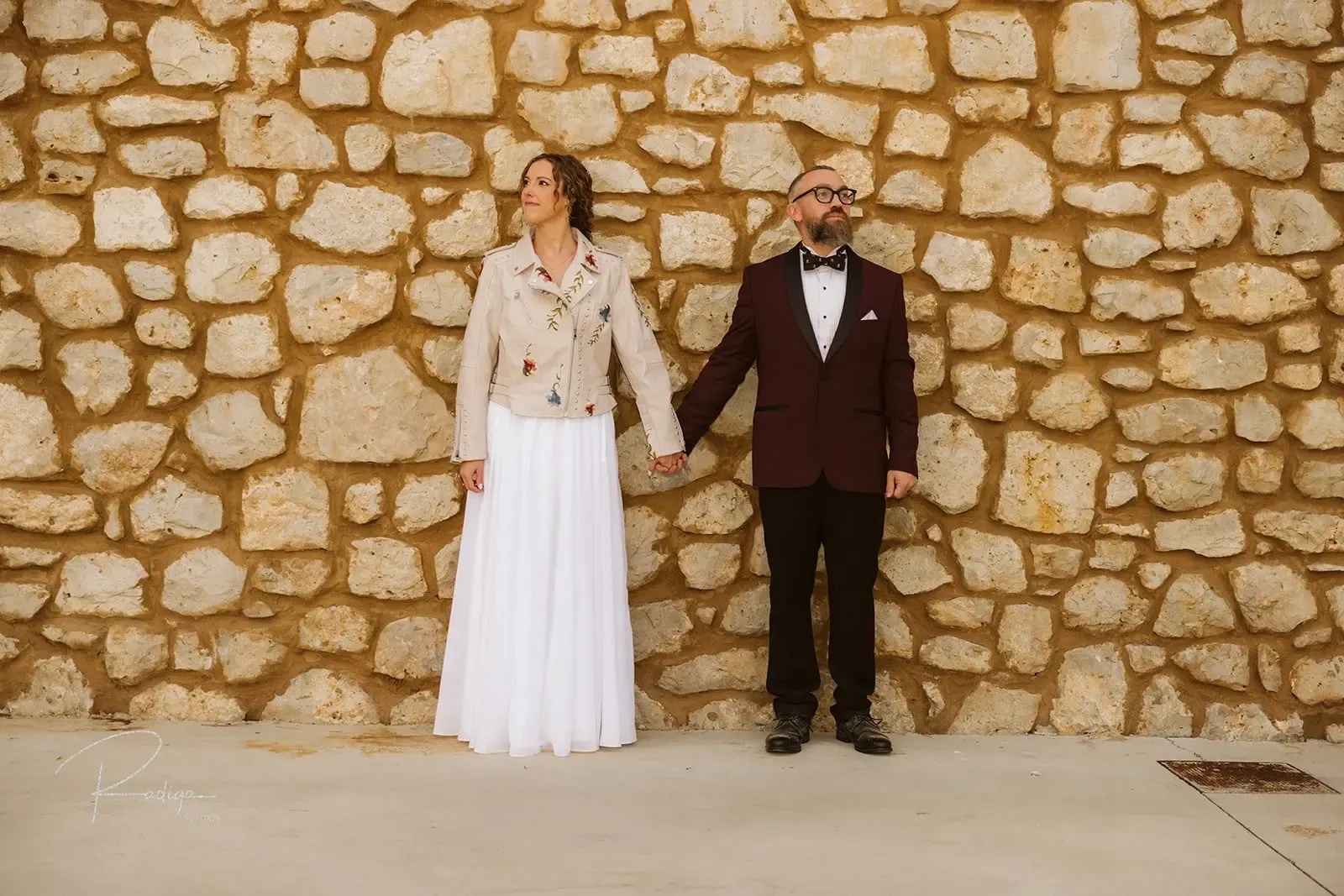 The couple holding hands against a stone wall at Arzuaga