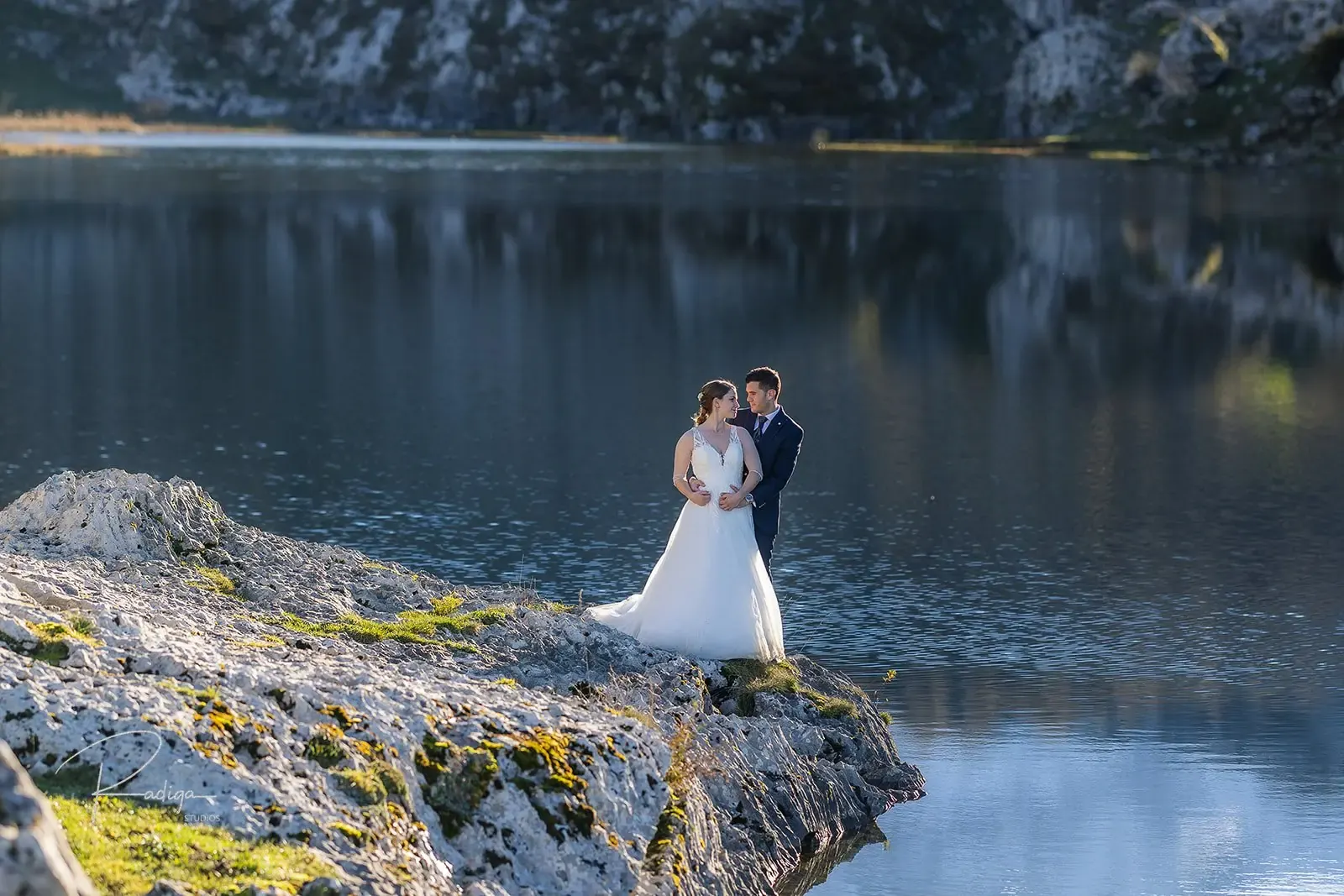 Los novios abrazados sobre las rocas a la orilla del lago