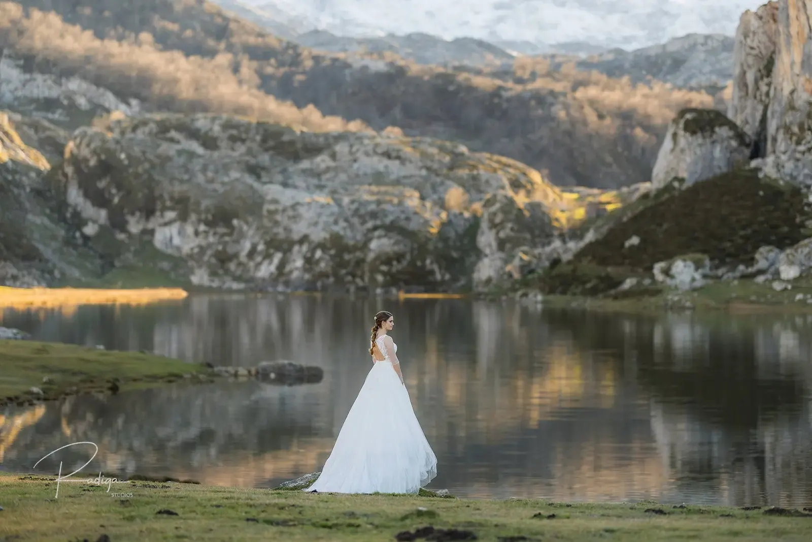 La novia se aleja por la pradera con el lago y las montañas reflejadas al fondo