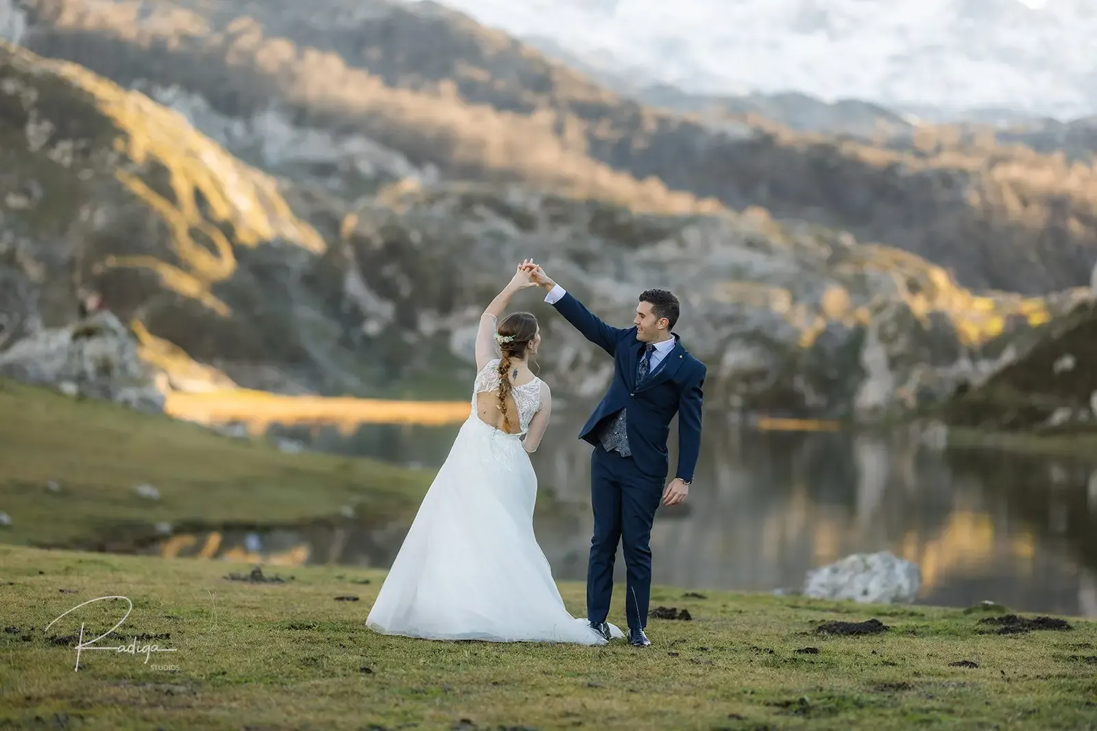 El novio hace girar a la novia en la pradera junto al lago