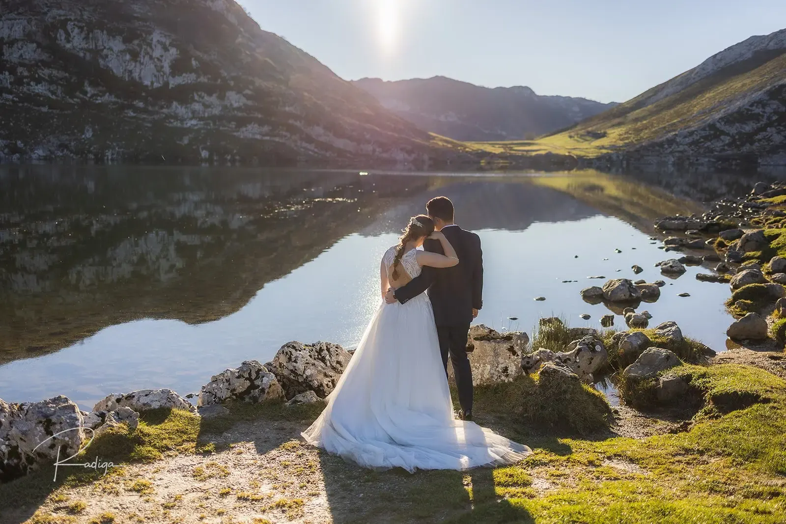 Los novios abrazados sobre las rocas con el lago y las montañas detrás