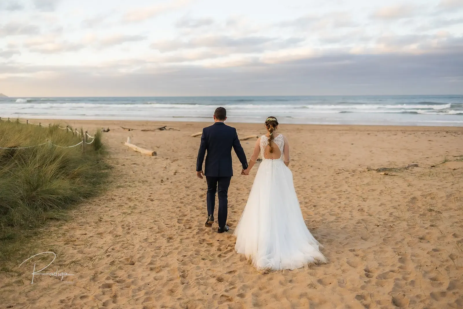 Los novios caminan por la arena hacia el mar en la playa de La Vega