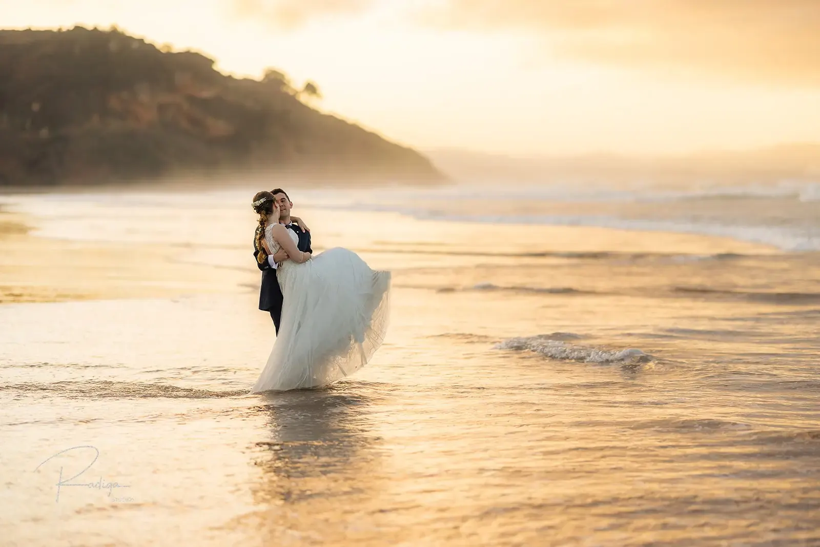 El novio levanta a la novia en la orilla del mar al atardecer