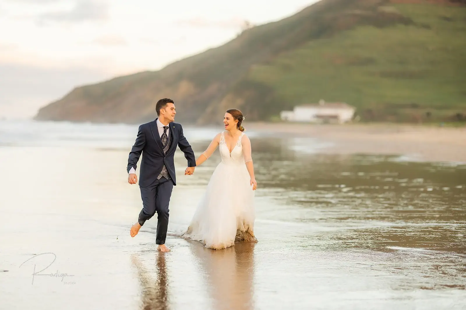 Los novios corren de la mano por la orilla de la playa