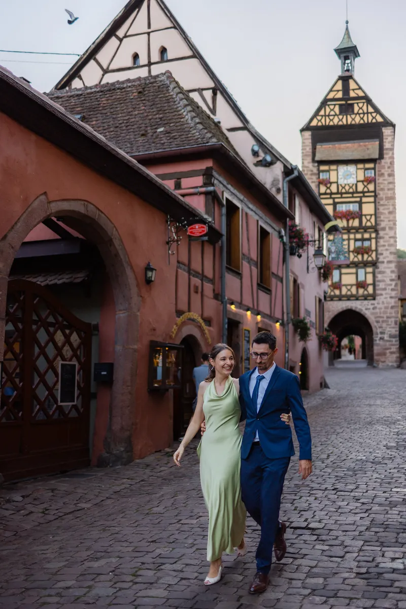 Víctor y Sandra paseando por una calle empedrada de Riquewihr, con la torre del Dolder al fondo