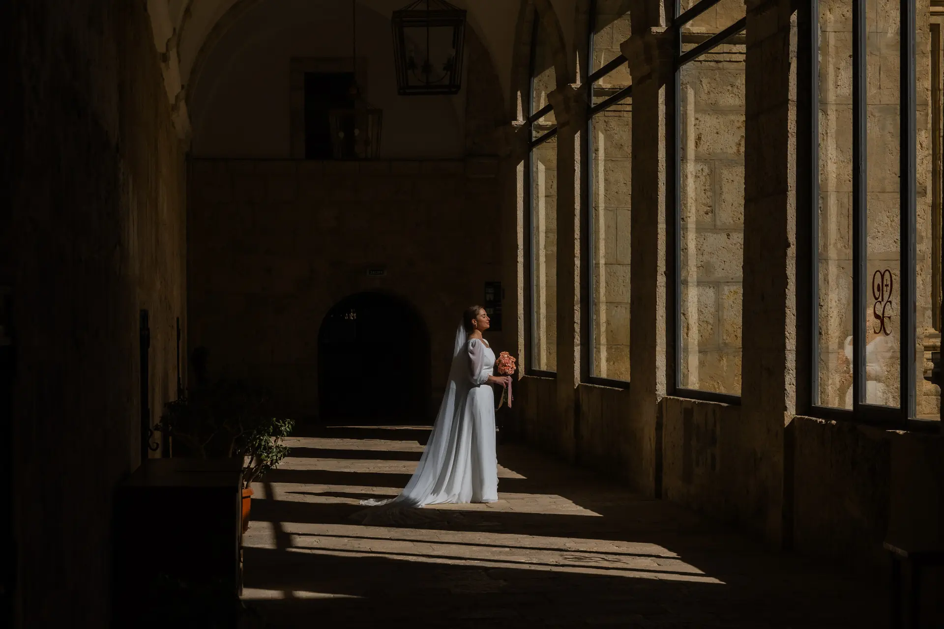 Novia con su ramo en el claustro de un monasterio, iluminada por la luz que entra por los ventanales