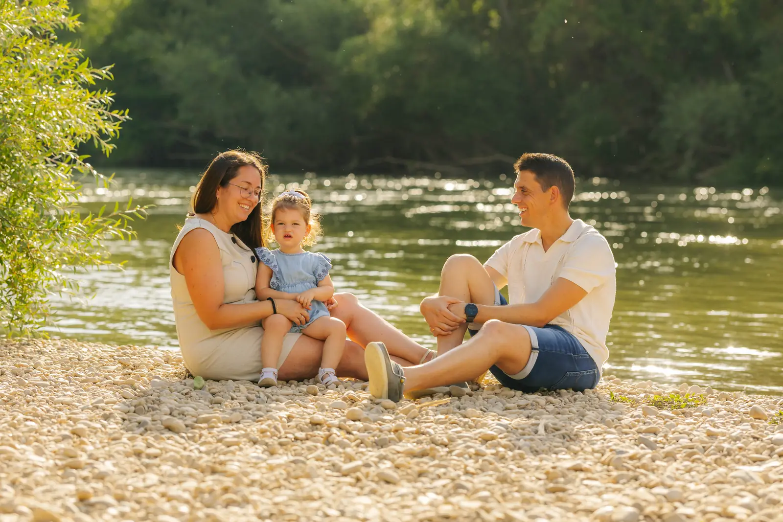 Padre, madre y su hija sentados en las piedras de la orilla del río al atardecer